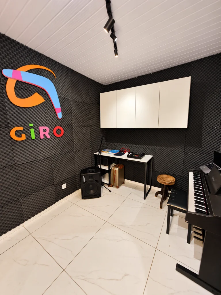 Estúdio musical com isolamento acústico, piano digital e logotipo da Escola Giro